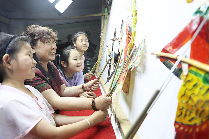 皮影藝人指導小朋友表演皮影戲。